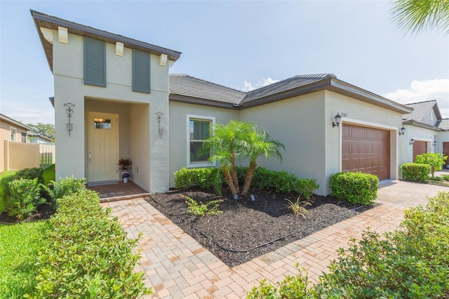 view of front facade featuring decorative driveway, fence, an attached garage, and stucco siding