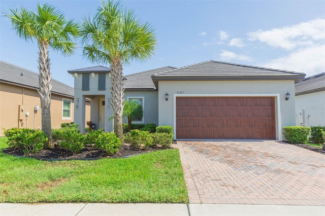 view of front of property with an attached garage, a tiled roof, decorative driveway, stucco siding, and a front yard