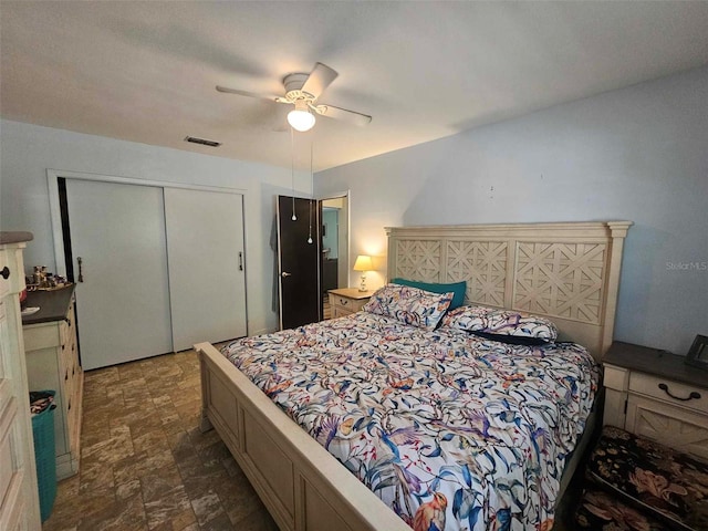 bedroom with ceiling fan, visible vents, a closet, and stone finish flooring