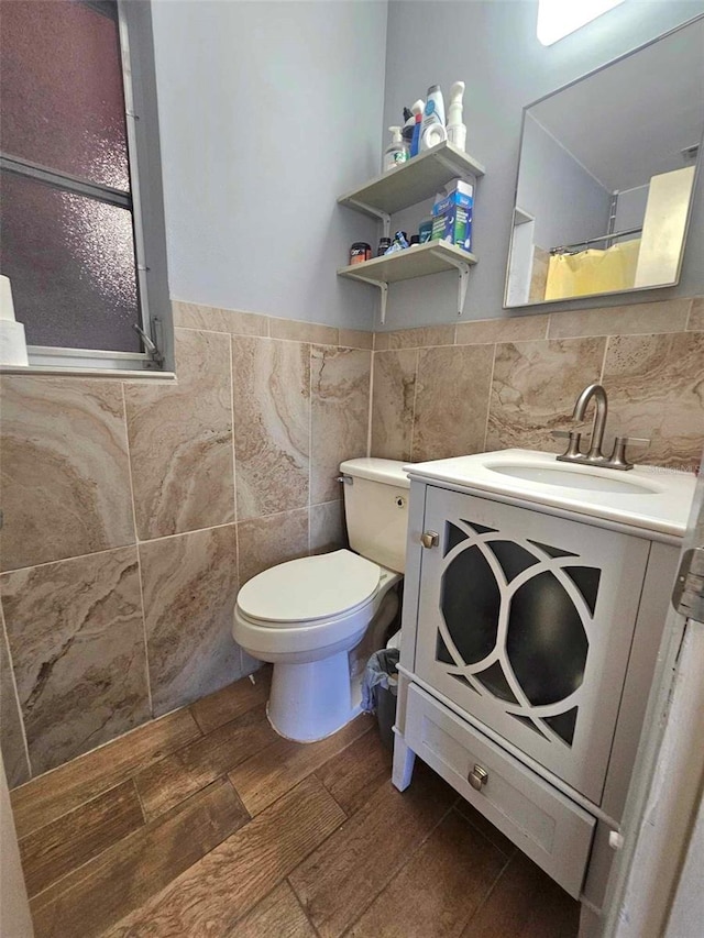 bathroom featuring toilet, a wainscoted wall, wood finished floors, vanity, and tile walls