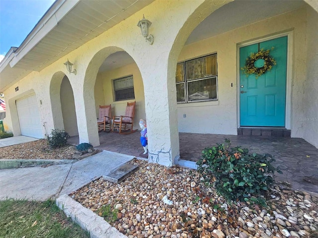 entrance to property with a garage, covered porch, and stucco siding