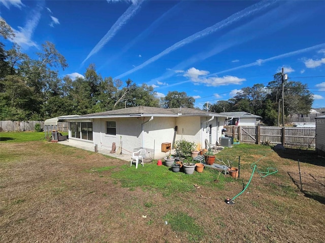 rear view of property featuring a yard, central AC, a fenced backyard, and stucco siding