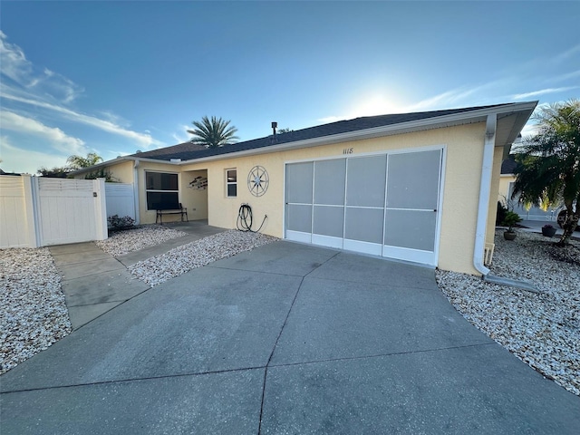 view of front of home with concrete driveway, an attached garage, a gate, fence, and stucco siding