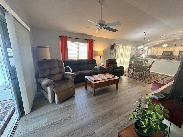 living area with vaulted ceiling, ceiling fan with notable chandelier, and light wood-type flooring