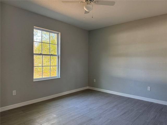 unfurnished room with dark wood-type flooring, ceiling fan, and baseboards