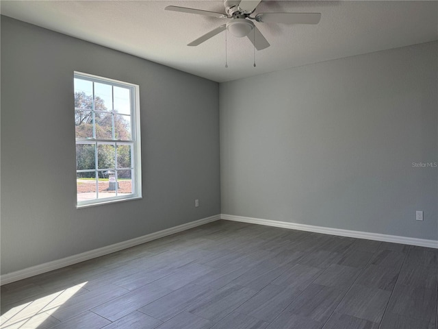 spare room featuring dark wood-style floors, ceiling fan, and baseboards