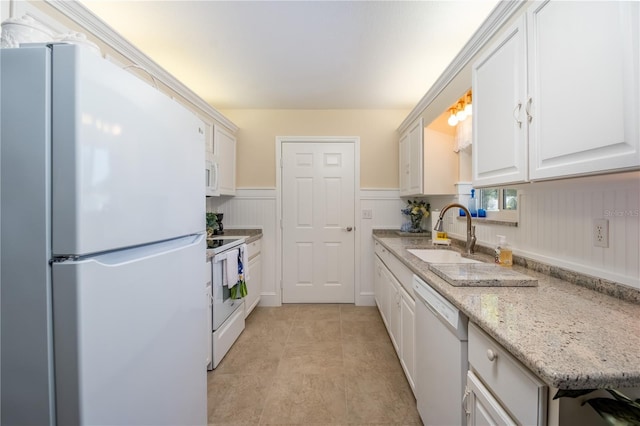 kitchen featuring white appliances, white cabinets, a sink, and wainscoting