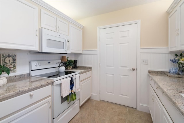 kitchen with a wainscoted wall, white cabinetry, light tile patterned flooring, light stone countertops, and white appliances