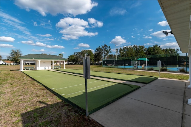 surrounding community featuring a tennis court, fence, and a lawn