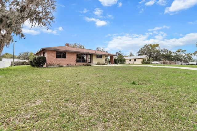 ranch-style home with a front yard, brick siding, fence, and a chimney