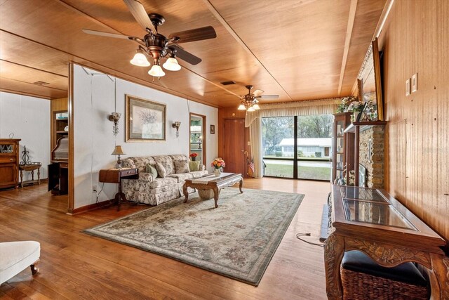 living area with ceiling fan, wooden walls, wood finished floors, visible vents, and wood ceiling