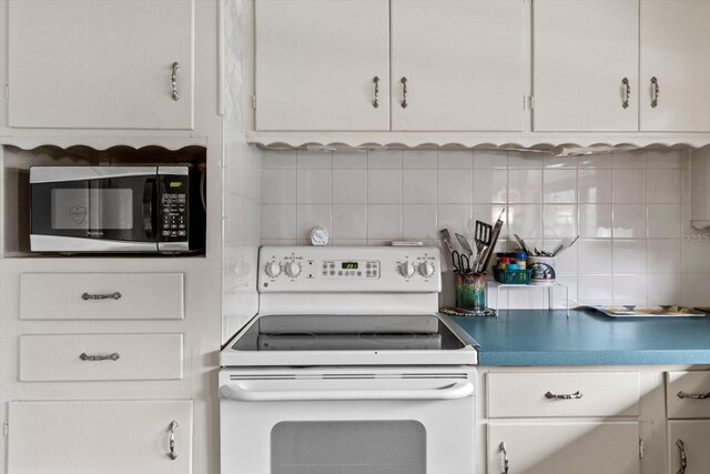 kitchen featuring white electric range, stainless steel microwave, backsplash, and white cabinets