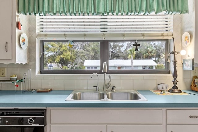 kitchen featuring dishwasher, tasteful backsplash, a sink, and white cabinets