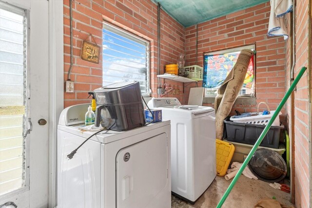 clothes washing area featuring brick wall, laundry area, and washing machine and dryer