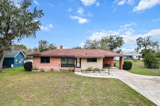 ranch-style house featuring brick siding, fence, driveway, a front lawn, and a chimney