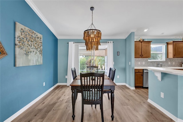 dining area with light wood finished floors, baseboards, ornamental molding, and an inviting chandelier