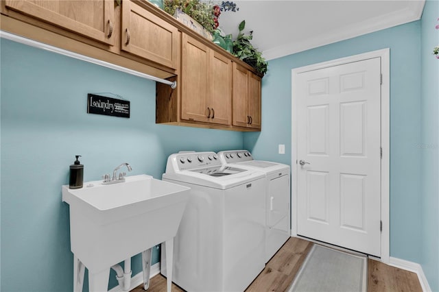 laundry area featuring cabinet space, baseboards, independent washer and dryer, light wood-type flooring, and a sink