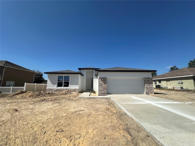 prairie-style home featuring concrete driveway, stone siding, an attached garage, fence, and stucco siding