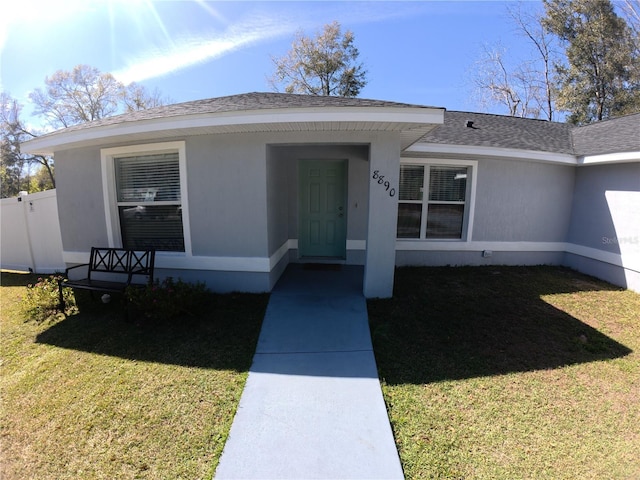 entrance to property with stucco siding, roof with shingles, fence, and a yard