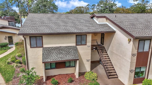 view of front of home with a shingled roof, stairway, and stucco siding