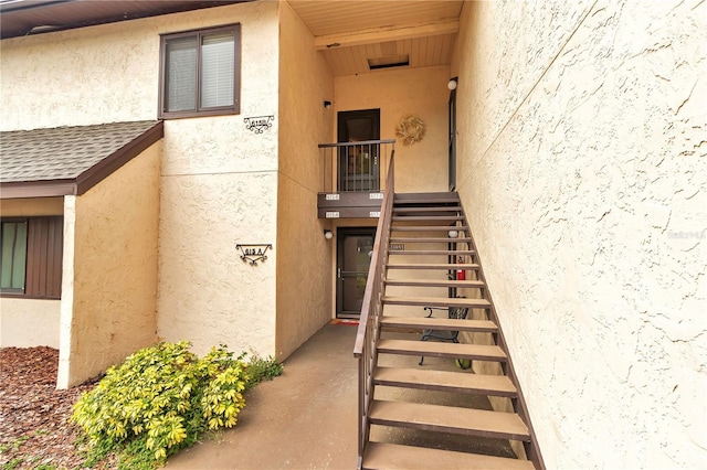 entrance to property featuring roof with shingles and stucco siding