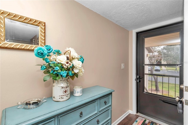 doorway to outside with dark wood-style floors, a textured ceiling, and baseboards