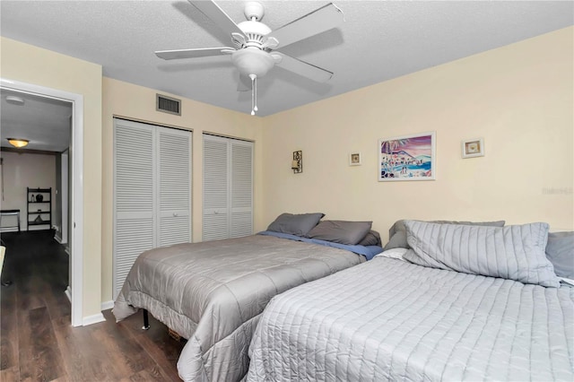 bedroom featuring a textured ceiling, visible vents, multiple closets, and wood finished floors