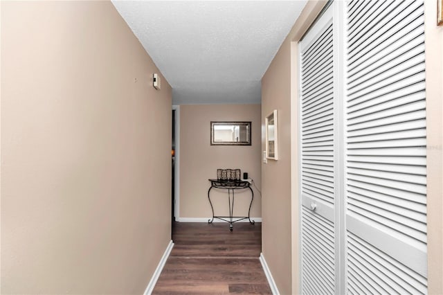 corridor with dark wood-style floors, a textured ceiling, and baseboards