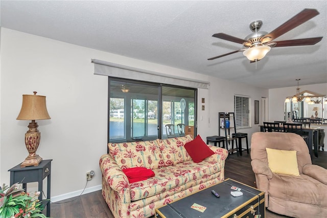 living area featuring a textured ceiling, ceiling fan with notable chandelier, dark wood finished floors, and baseboards