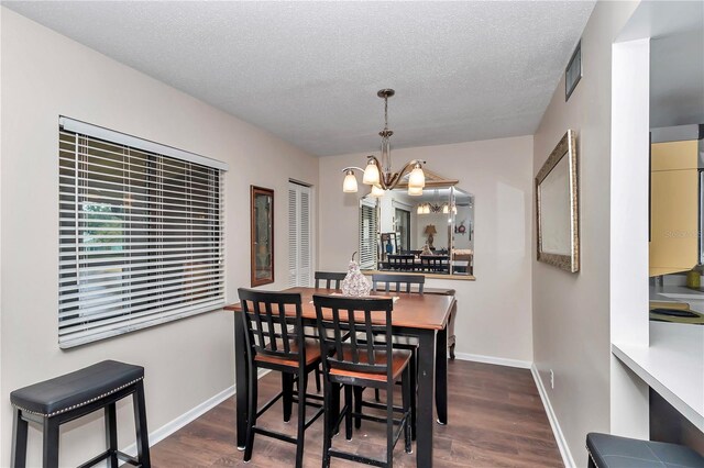 dining space with visible vents, a textured ceiling, wood finished floors, a chandelier, and baseboards