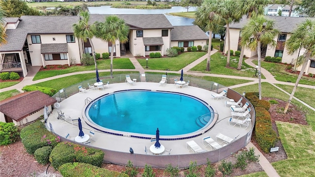 pool with a lawn, a patio area, fence, and a water view