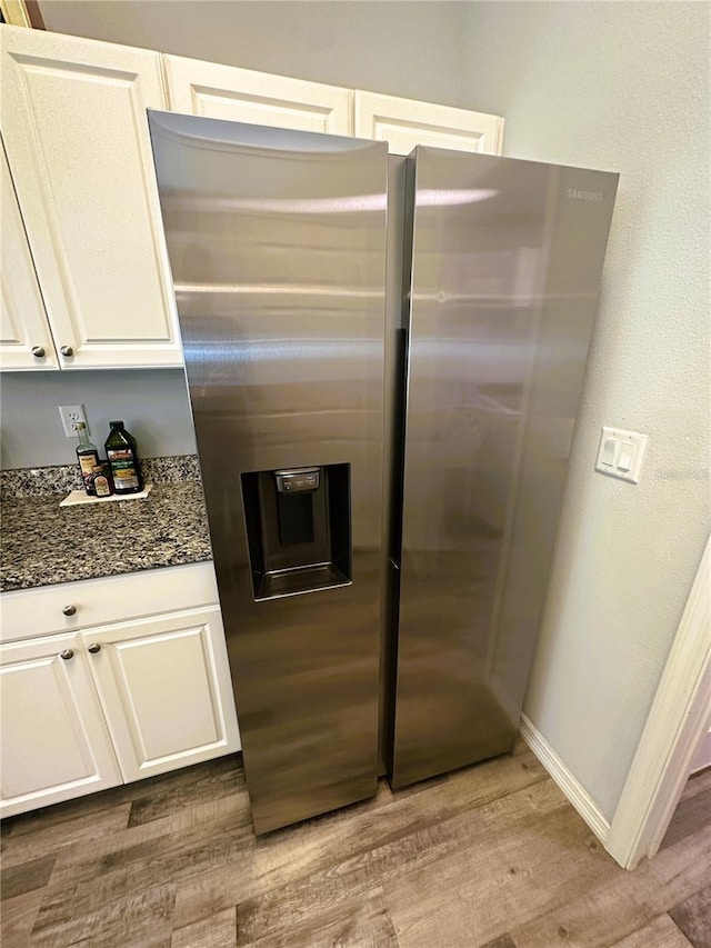 kitchen featuring dark stone counters, light wood-type flooring, stainless steel fridge, and white cabinetry