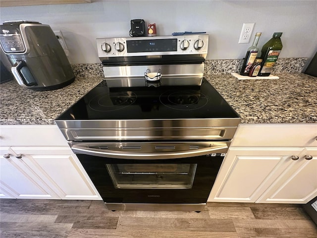 kitchen with dark stone counters, white cabinetry, and stainless steel electric stove