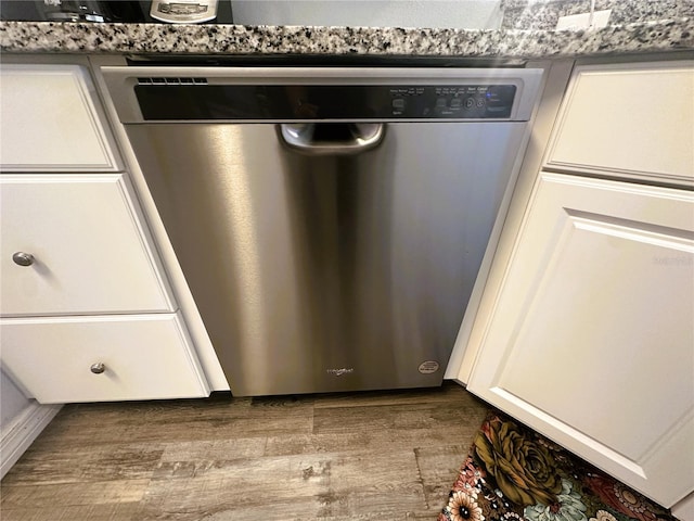 interior details featuring white cabinets, stainless steel dishwasher, and wood finished floors