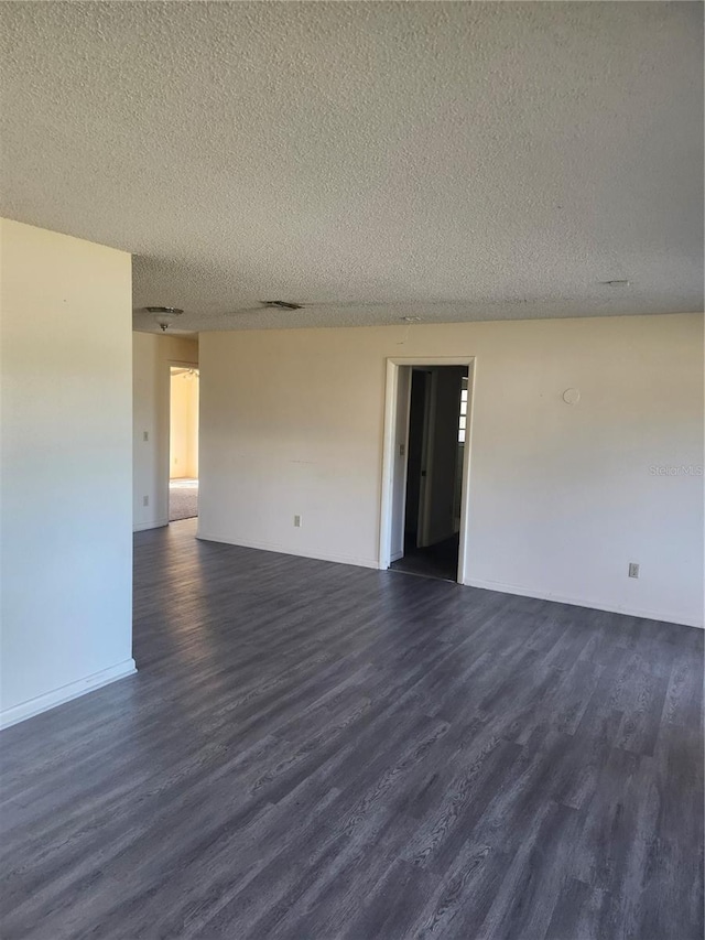 empty room with a textured ceiling, visible vents, and dark wood-style flooring