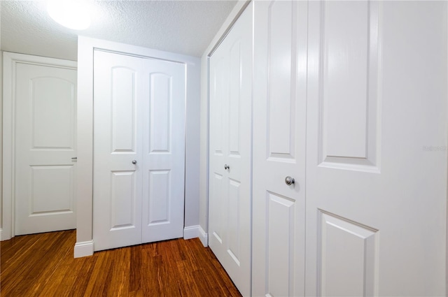 hall featuring a textured ceiling, dark wood finished floors, and baseboards