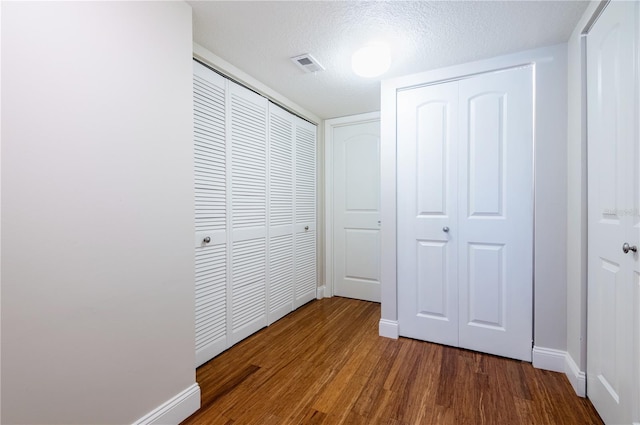 corridor with visible vents, a textured ceiling, baseboards, and wood finished floors