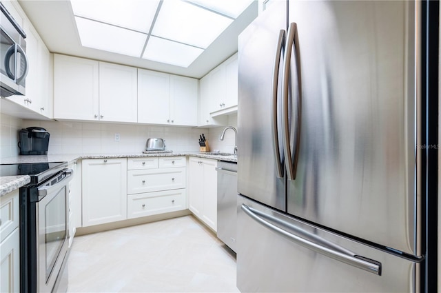 kitchen with light stone counters, a sink, white cabinets, appliances with stainless steel finishes, and decorative backsplash