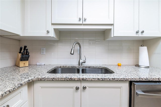 kitchen with tasteful backsplash, a sink, white cabinetry, and light stone countertops