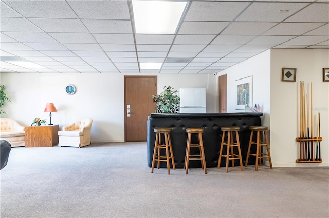 bar featuring a drop ceiling, baseboards, freestanding refrigerator, a bar, and carpet