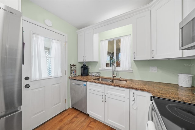 kitchen with dark stone counters, appliances with stainless steel finishes, light wood-type flooring, white cabinetry, and a sink