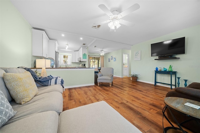 living area with ceiling fan, wood finished floors, visible vents, and baseboards