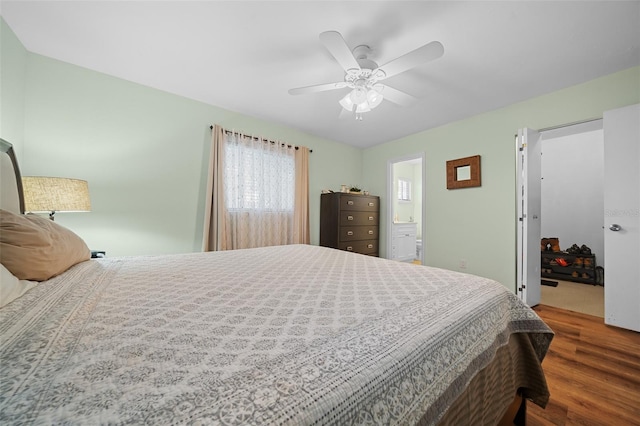 bedroom featuring connected bathroom, wood finished floors, a ceiling fan, and a walk in closet