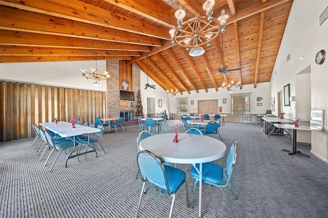 carpeted dining area featuring wooden ceiling, beamed ceiling, a fireplace, high vaulted ceiling, and ceiling fan with notable chandelier