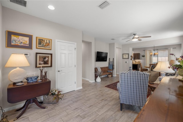 living area with light wood finished floors, baseboards, visible vents, and ceiling fan with notable chandelier