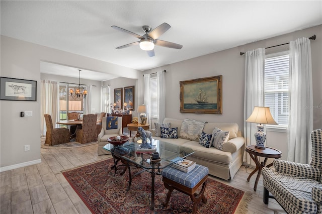 living room featuring ceiling fan with notable chandelier, baseboards, a wealth of natural light, and light wood-style floors