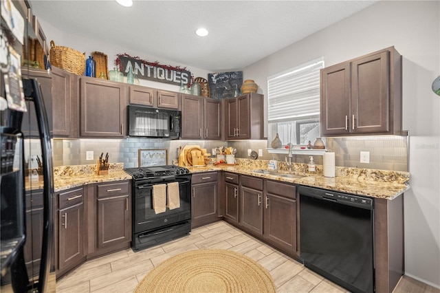 kitchen featuring decorative backsplash, light stone countertops, wood finish floors, black appliances, and a sink