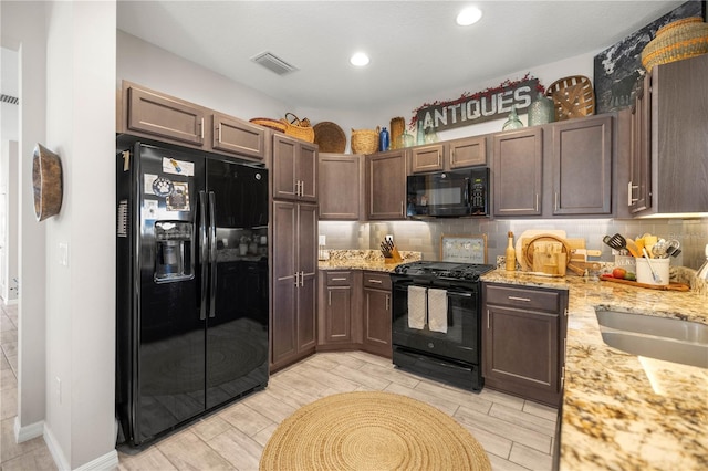 kitchen featuring light stone counters, a sink, visible vents, black appliances, and tasteful backsplash