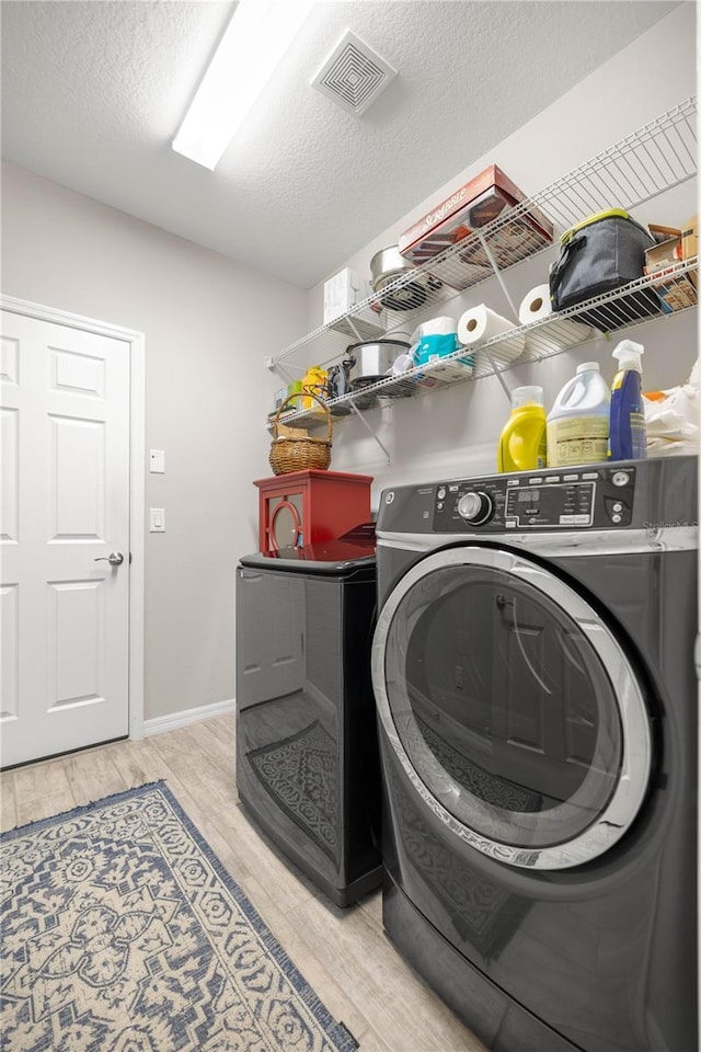 laundry area featuring a textured ceiling, light wood-style flooring, laundry area, visible vents, and independent washer and dryer