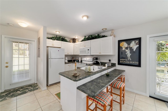 kitchen featuring light tile patterned floors, a peninsula, white appliances, a sink, and a wealth of natural light